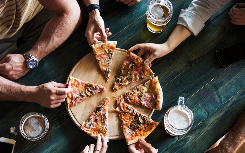 hands all grabbing for pizza on table